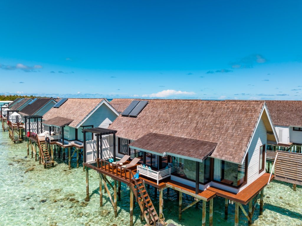 Mehrere Wind Villen auf Stelzen mit weißen Wänden und Holzschindeldächern über türkisfarbenem Wasser in Ozen Life Maadhoo