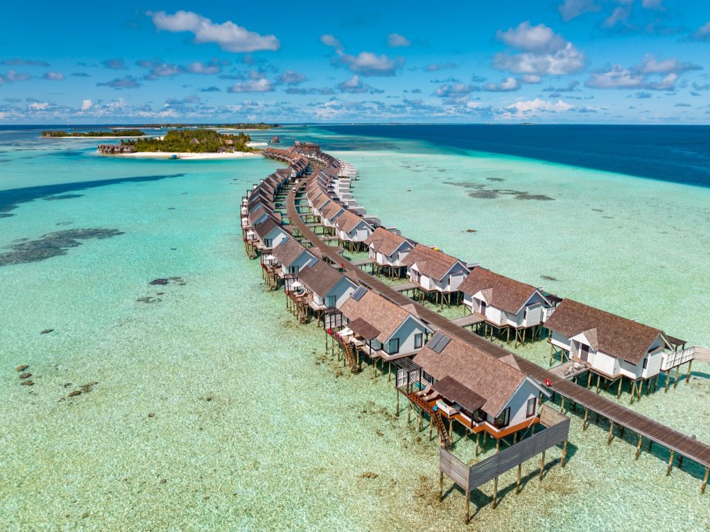 Wasserbungalows auf Stelzen mit strohgedeckten Dächern über türkisfarbener Lagune, verbunden durch hölzerne Stege