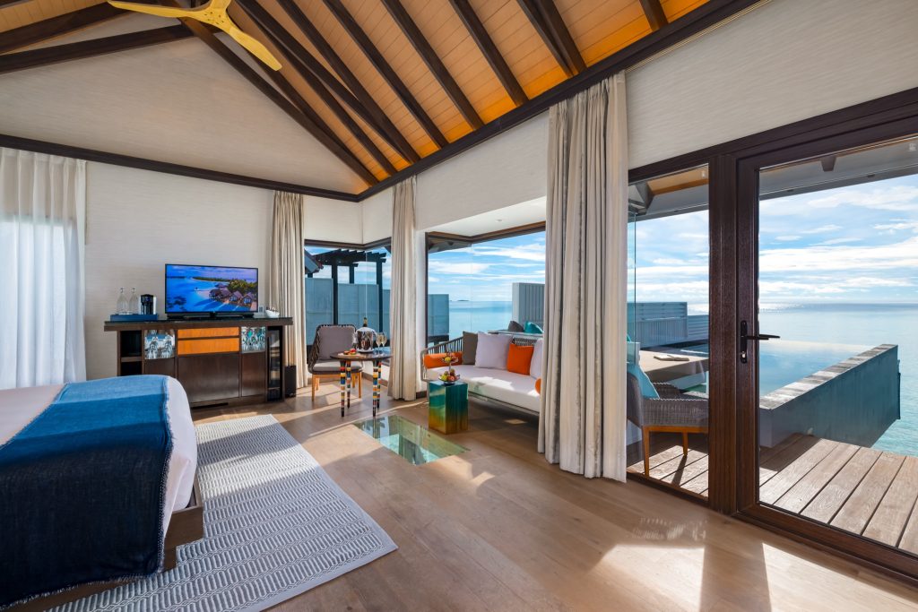 Zimmer der Wind Villa mit großem Bett, Holztischen, Fernseher und offenem Meerblick bei Tageslicht
