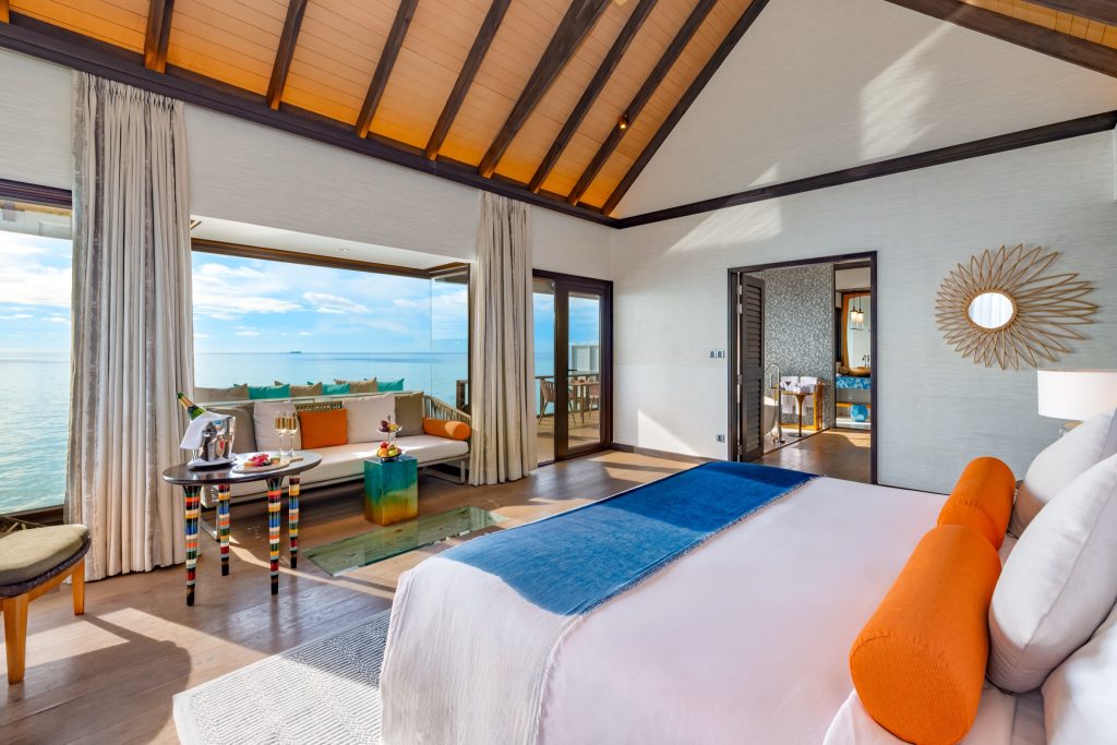 Wind Villa with Pool Zimmer mit großem Bett, Champagner auf Tisch, Holzboden und Meerblick durch Fenster im Ozen Life Maadhoo