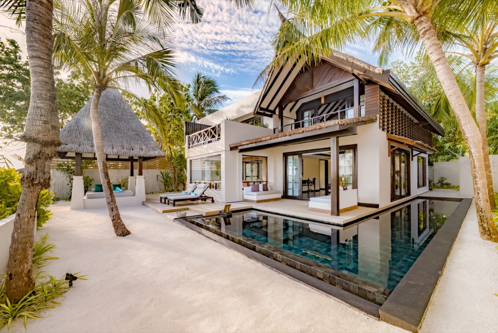 Strandvilla Earth Pool Reserve mit dunklem Pool, Holzterrasse, weißen Liegen und Palmen auf den