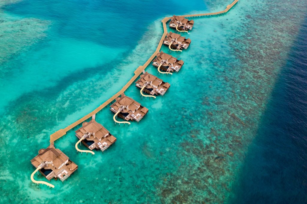 Überwasser-Bungalows mit Holzplattformen und braunen Dächern auf türkisfarbenem Wasser bei Tageslicht