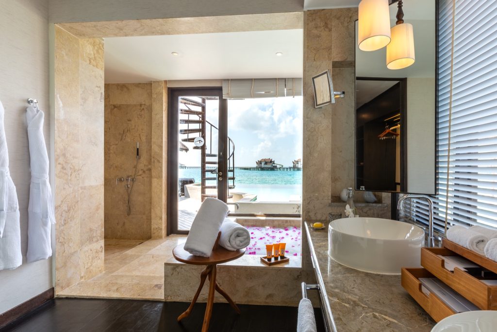 Badezimmer mit hellem Marmor, rundem weißen Waschtisch und Zugang zur Terrasse mit Meerblick in der Ocean Pool Suite
