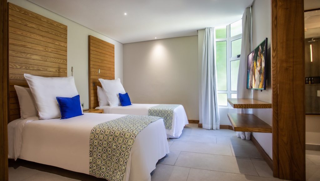 Modernes family Zimmer mit zwei Einzelbetten, hellem Holz, weißen Bettdecken und blauen Kissen im Paradis Beachcomber Golf.