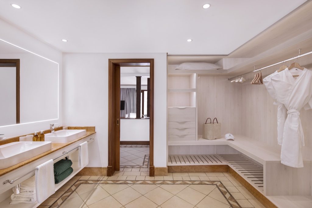 Heller Ankleideraum und Badezimmerbereich mit Marmorwaschbecken und Holzkleiderschrank in Junior Suite
