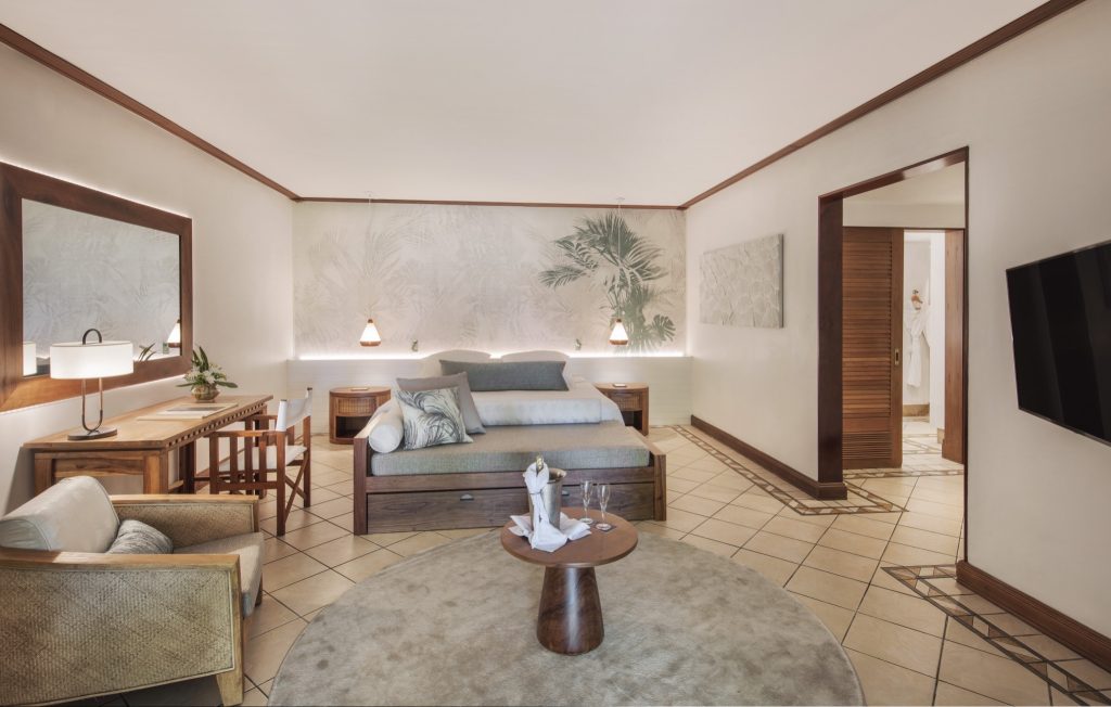 Helles Junior Suite Schlafzimmer mit großem Bett, Holzmöbeln, Schreibtisch und tropischer Wandtapete im Paradis Beachcomber