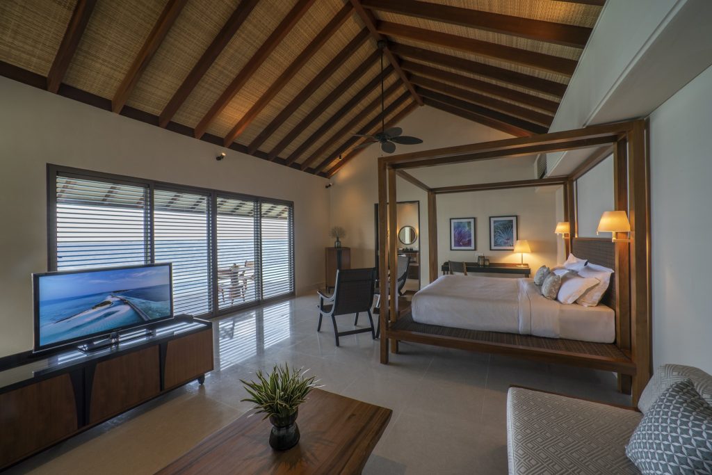 Geräumiges Zimmer der Deluxe Lagoon Pool Villa mit Holzdach, Himmelbett, Steinboden und Balkon auf den