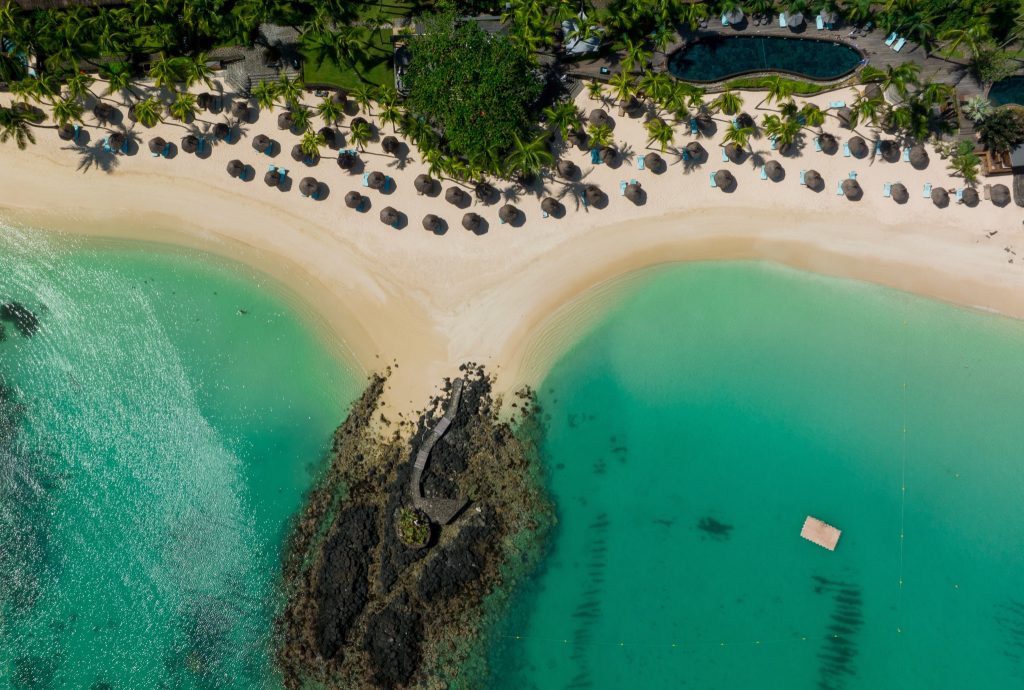 Vogelperspektive auf Strand mit halbkreisförmigen Liegestühlen, Strohschirmen, Palmen und türkisfarbenem Wasser in Mauritius