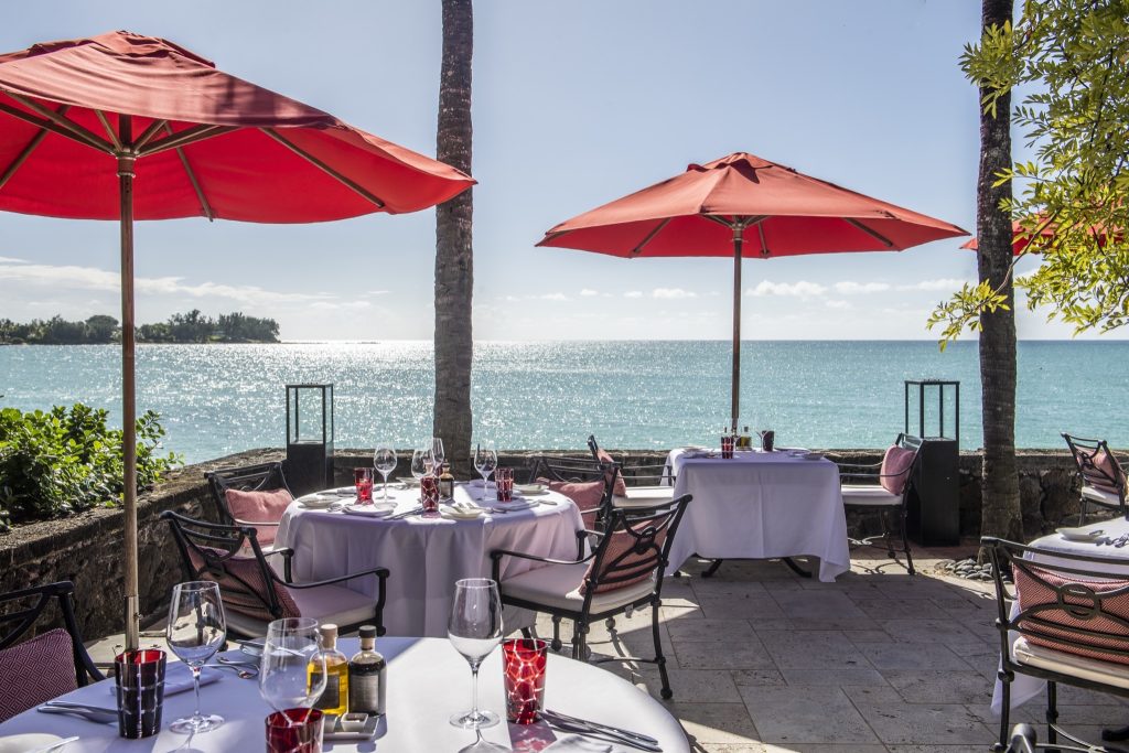 Terrasse des Restaurants Asiya mit weißen Tischdecken, roten Sonnenschirmen und Metallstühlen mit roten Kissen, Meerblick