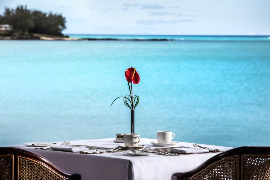 Tisch im Restaurant Goelette mit weißem Tischtuch, zwei Kaffeetassen, roter Blume und türkisblauem Meer im Hintergrund