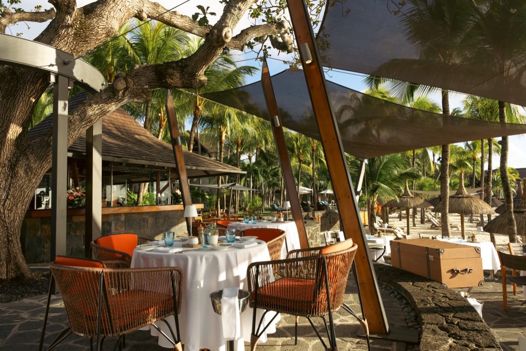 Außenterrasse des Restaurants Grand Sable mit gedecktem Tisch, Rattanstühlen und Sonnensegeln bei Tageslicht