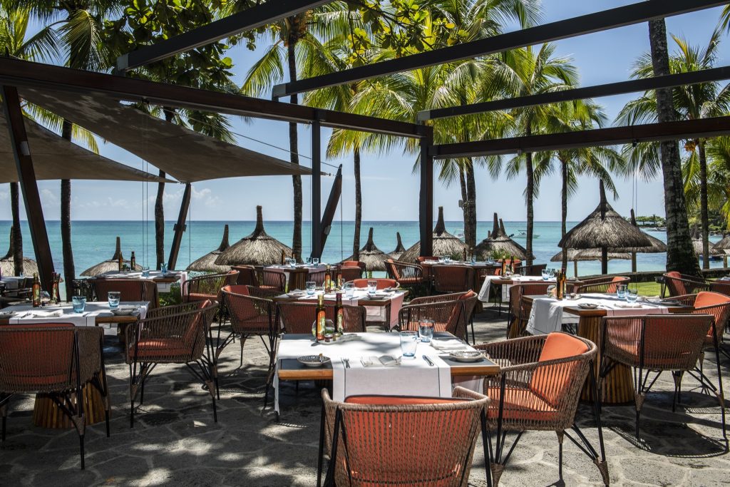 Open-Air-Terrasse des Restaurants La Plage mit Holzmöbeln, orangen Polstern und weißen Tischläufern am Meer