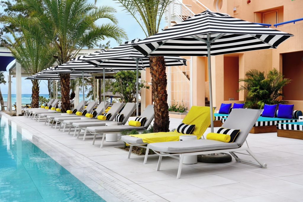 Poolbereich im Salt of Palmar mit hellgrauen Sonnenliegen, gelben Handtüchern, gestreiften Sonnenschirmen und Blick auf das.