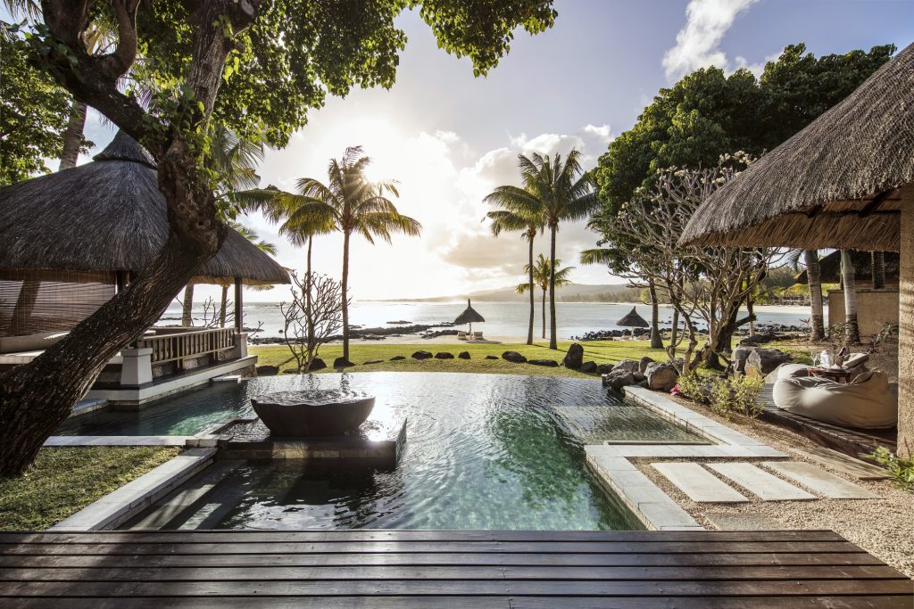 Poolbereich mit Holzdielen und Natursteinen, Palmen und Strohdach-Pavillon am Meer im Shanti Maurice Resort & Spa
