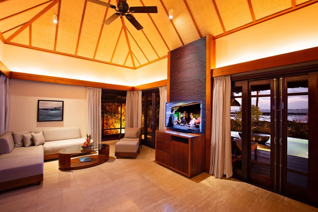 Heller Wohnbereich der Beachfront Suite Pool Villa mit Holzdecke, großer Fensterfront, moderner Couch und Blick auf Pool