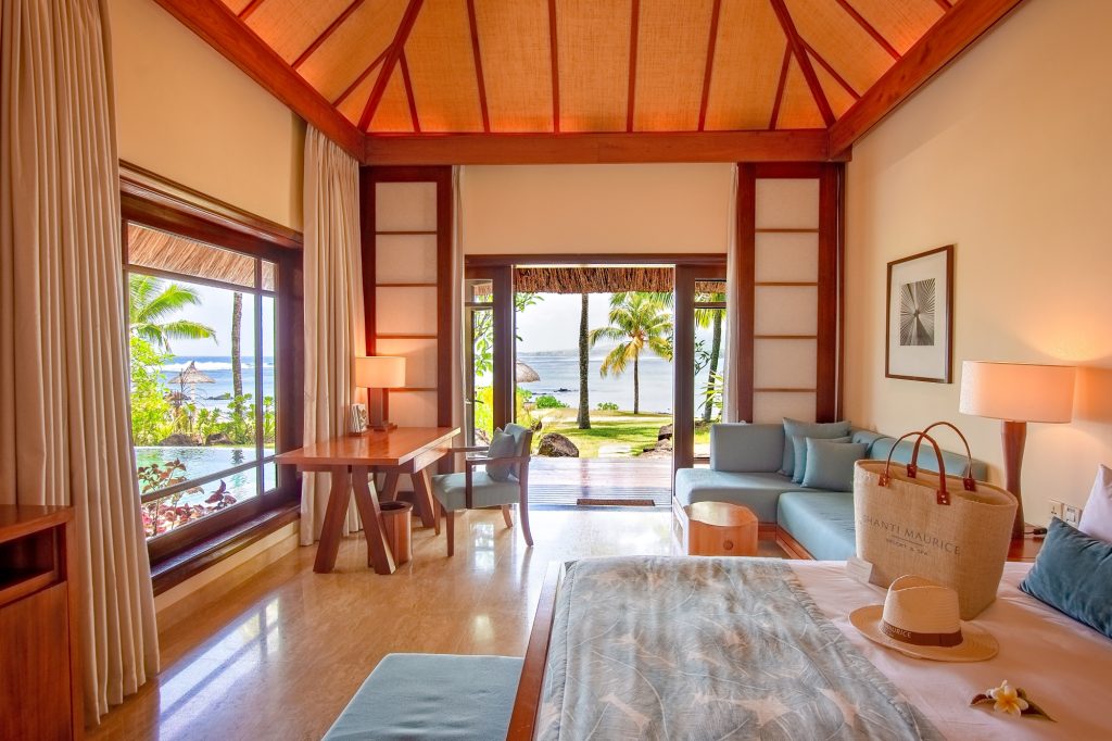 Zimmer der Beachfront Suite Pool Villa mit Holzmöbeln, blauen Polstermöbeln und Blick auf Terrasse und tropische Palmen