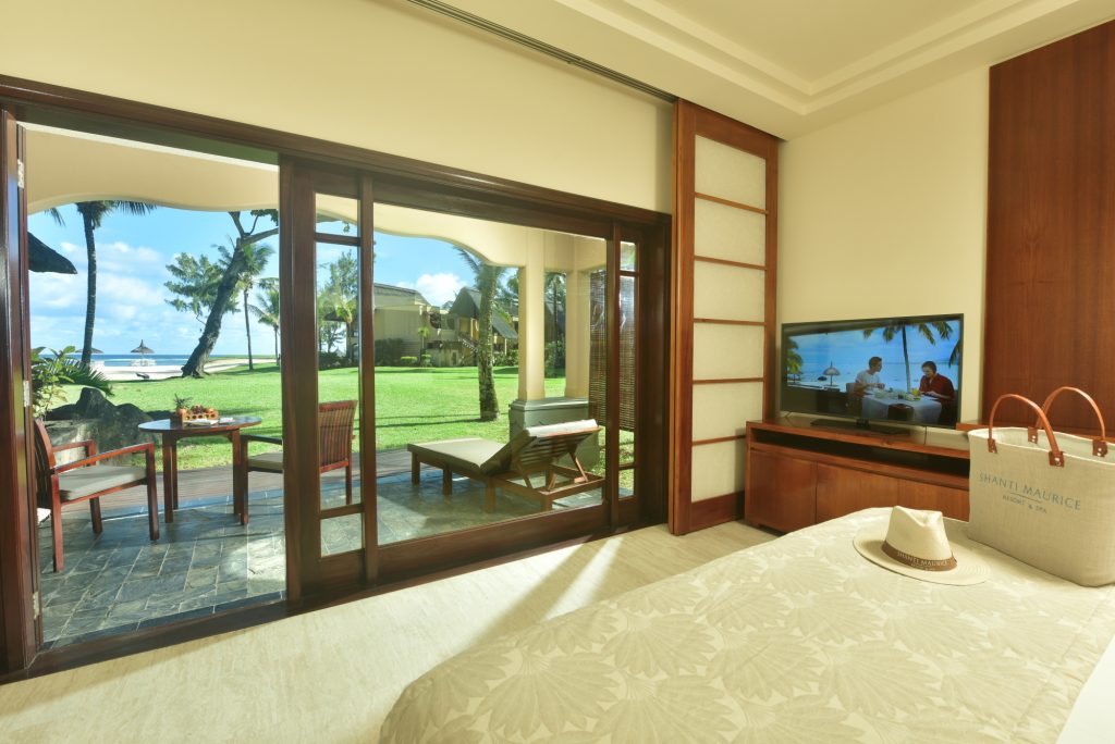Junior Suite Oceanview mit Bett, Holz-Fernsehtisch, Terrasse mit Tisch und Stühlen, Blick auf Rasen und Meer