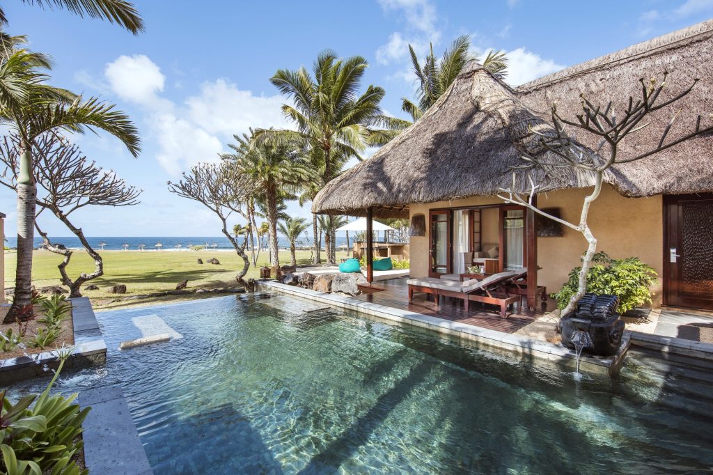 Poolvilla mit strohgedecktem Dach, Holzarchitektur und kleinem Pool vor tropischer Küstenlandschaft auf Mauritius