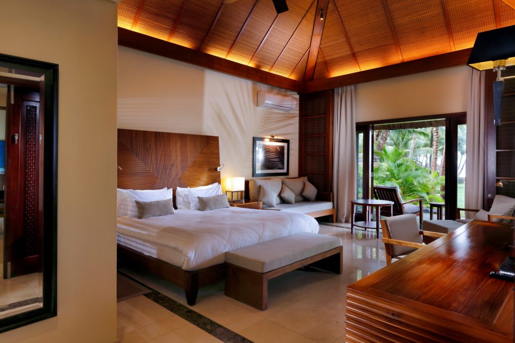 Geräumiges Hotelzimmer mit großem Doppelbett, Sitzgruppe und Blick auf Garten mit Palmen in Mauritius