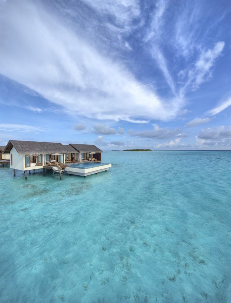 Luftaufnahme eines über Wasser auf Stelzen gebauten Resorts mit Strohdächern und türkisfarbenem Wasser auf den