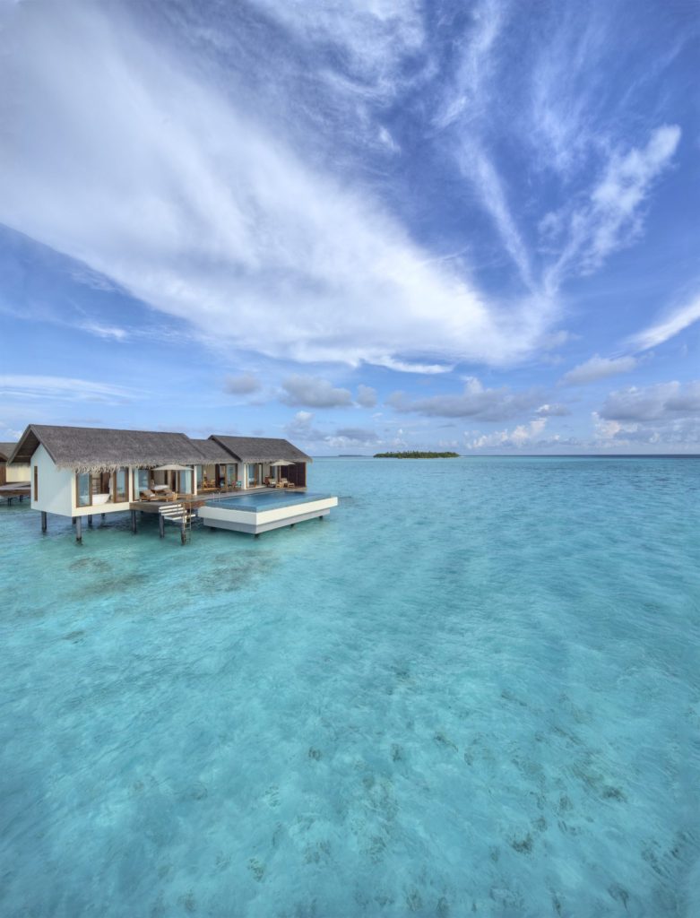 Luftaufnahme eines über Wasser auf Stelzen gebauten Resorts mit Strohdächern und türkisfarbenem Wasser auf den