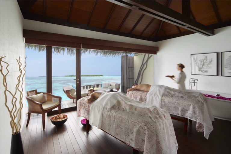 Wellness Spa mit zwei Massageliegen, weißen Überwürfen, großem Fenster und Blick auf das türkisfarbene Meer