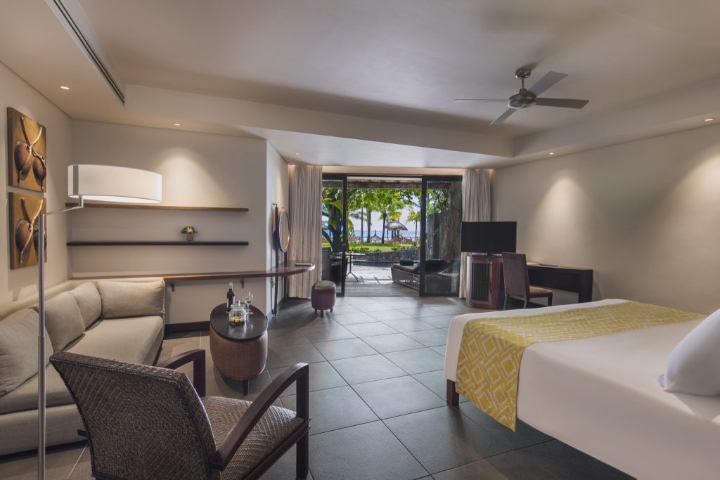 Modernes Hotelzimmer der Beachfront Suite mit Sofa, Tisch, Holzregalen und Blick auf Terrasse und Strand