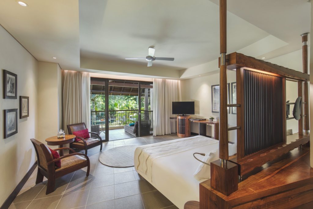 Geräumiges Junior Suite Zimmer mit großem Bett, Holz- und Rattanmöbeln und Balkon mit Blick auf tropisches Grün