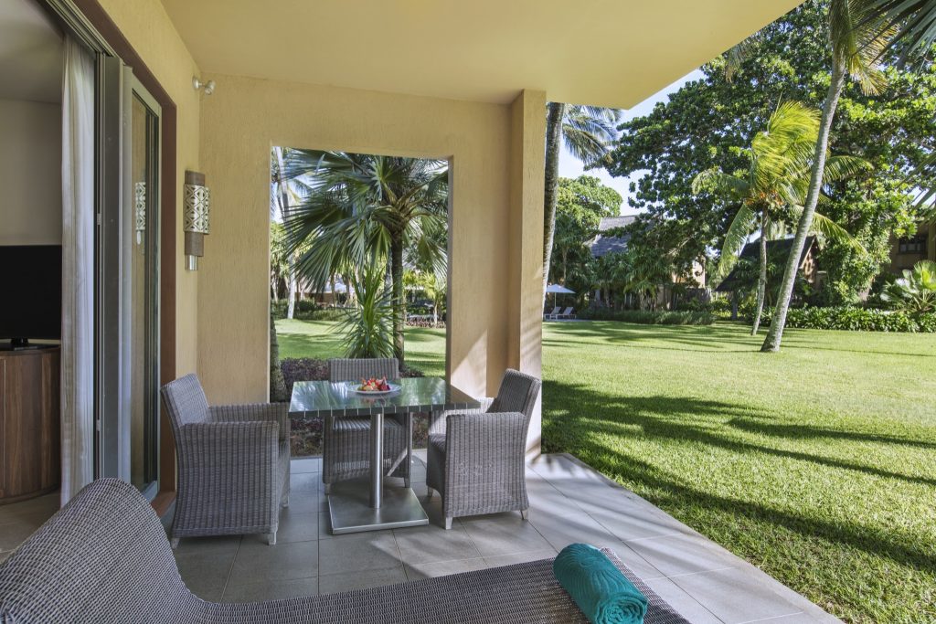 Terrasse der Junior Suite mit geflochtenen Rattansesseln und gläsernem Tisch, Blick auf Grünflächen und Palmen