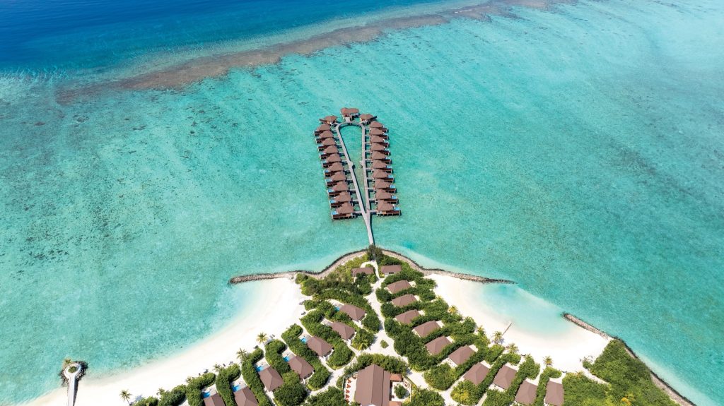Luftaufnahme eines Resorts auf den Malediven mit Steg und Holzbungalows über türkisfarbenem Wasser