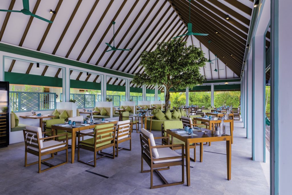 Offener Restaurantbereich Lime and Chili mit Holz- und grünen Stoffmöbeln, Glaswänden und Blick auf Vegetation