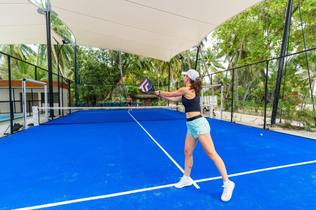 Padelplatz mit blauem Boden, hohem Gitterzaun und Sonnensegel umgeben von Palmen im Veligandu Maldives Resort Island