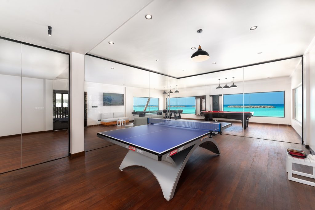 Moderner Sport- und Spielraum mit Tischtennistisch, Billardtisch, dunklem Holzboden und Blick auf Strand und Meer
