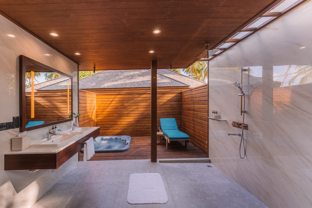 Offener Badezimmerbereich der Beach Villa mit zwei Waschbecken, großem Spiegel und Außenbereich mit Whirlpool