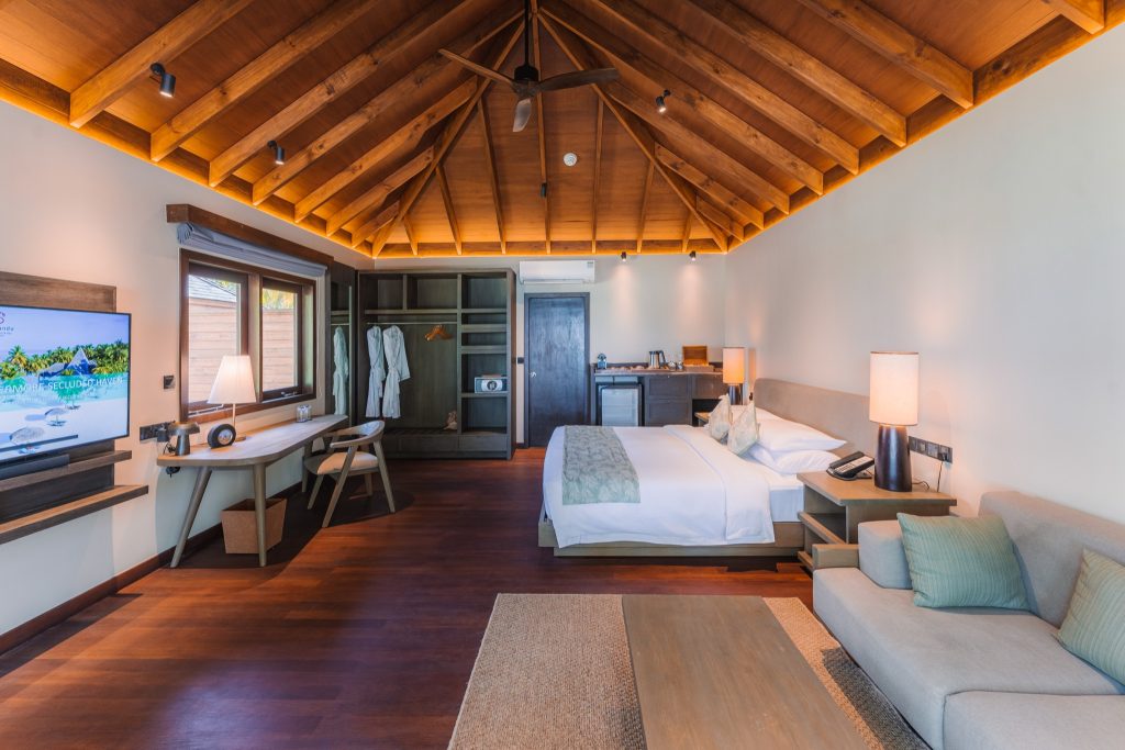 Geräumiges Zimmer der Beach Villa mit offenem Holzdach, großem Bett, Schreibtisch und Blick auf Außendeck
