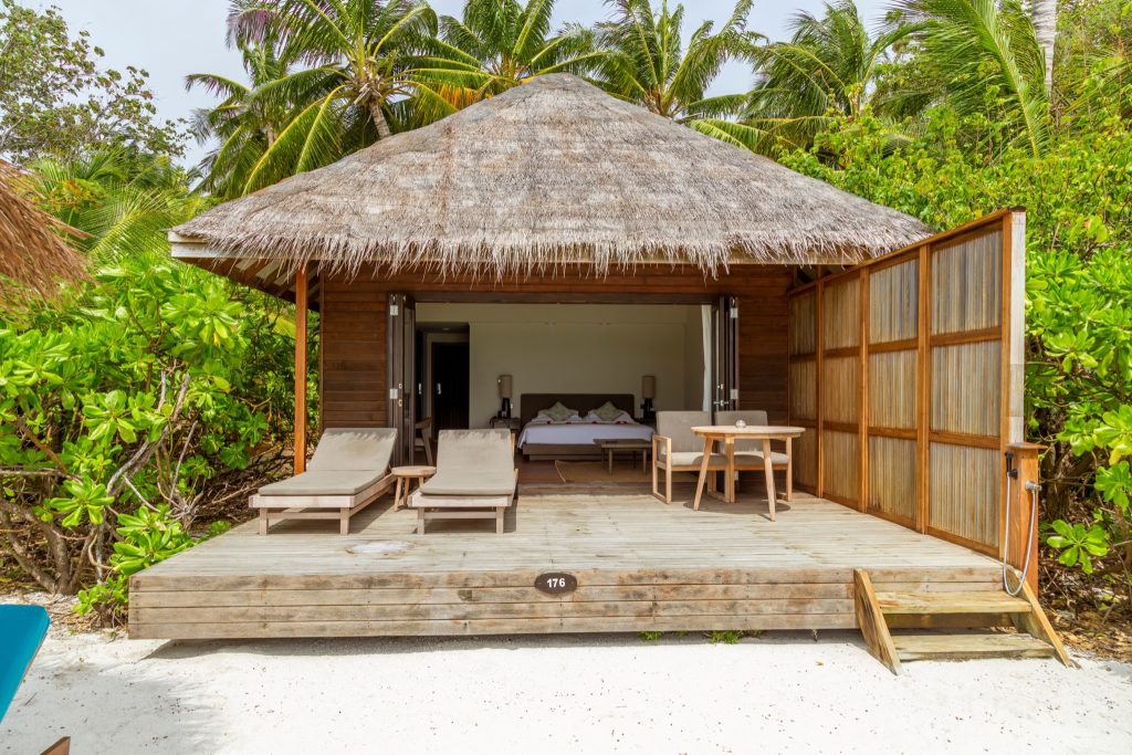 Strandhütte mit offenem Holzdesign, Strohdach, Sonnenliegen und Blick auf das Bett innen