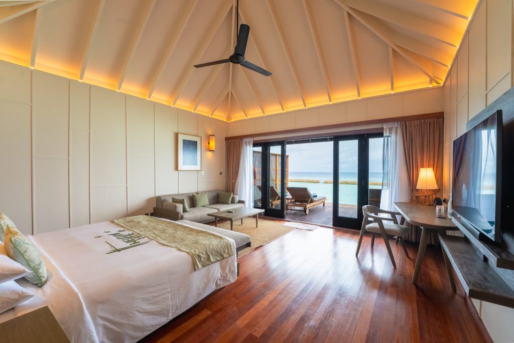 Zimmer der Ocean Jacuzzi Villa mit großem Bett, Ecksofa, dunklem Holzboden und Terrasse mit Meerblick