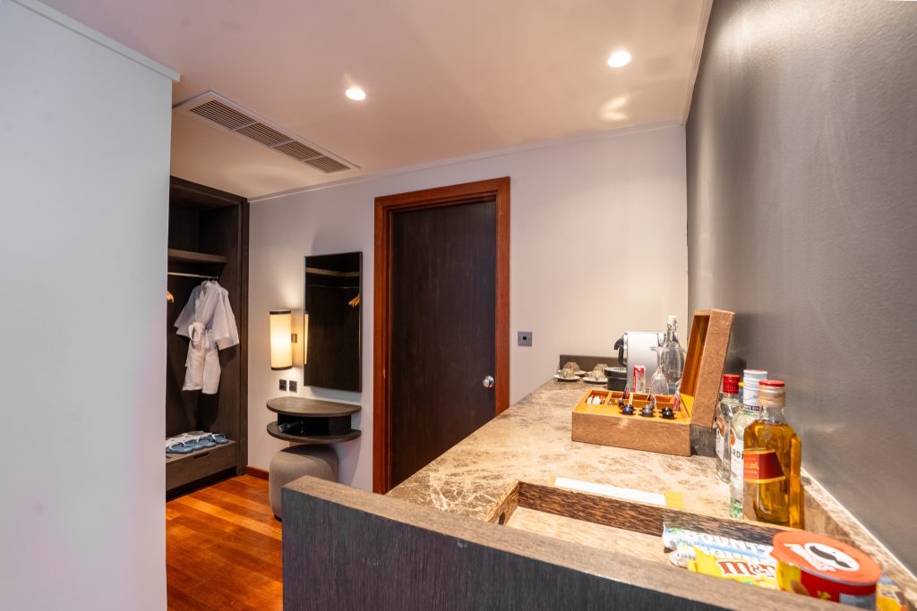 Hotelzimmer mit Marmor-Anrichte, Getränken, Snacks, Holzboden und offenem Kleiderschrank mit Bademantel
