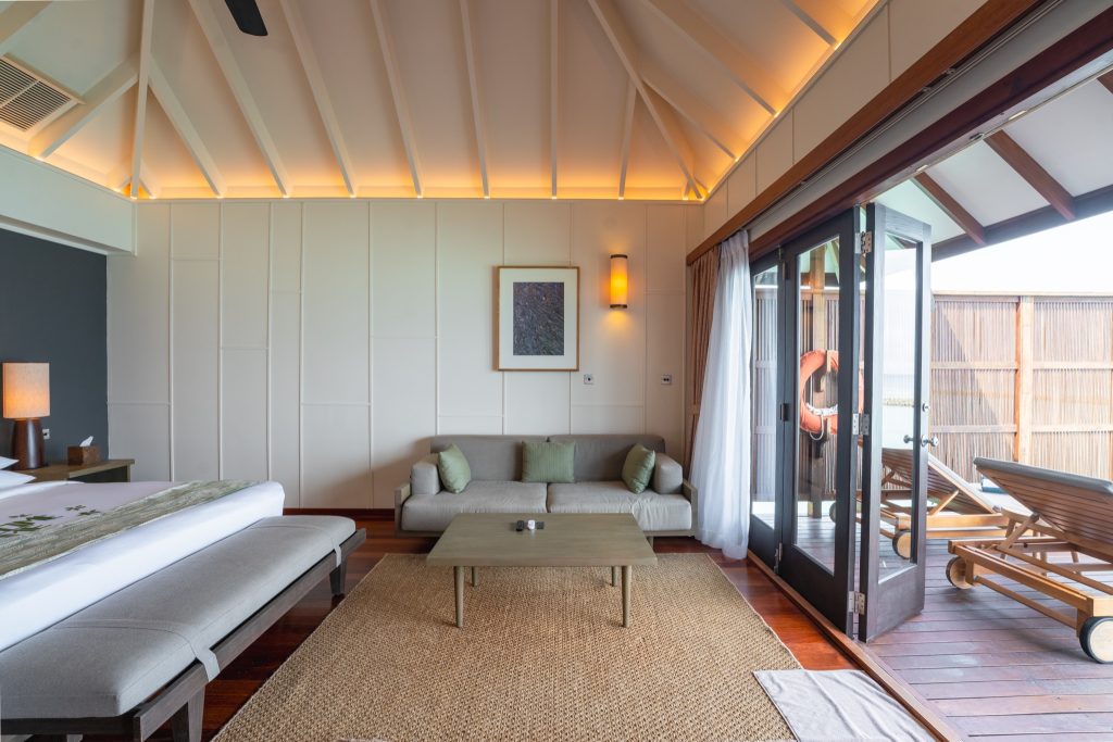 Helles Ocean Jacuzzi Villa Zimmer mit Sofa, grünem Kissen, Holzboden und Terrasse