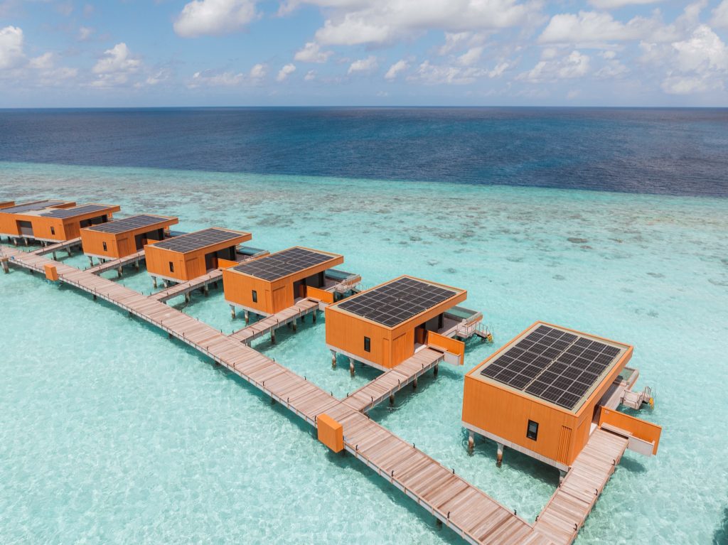 Überwasser-Bungalows mit flachen Dächern und Solarpaneelen auf Holzstegen im türkisfarbenen Meer