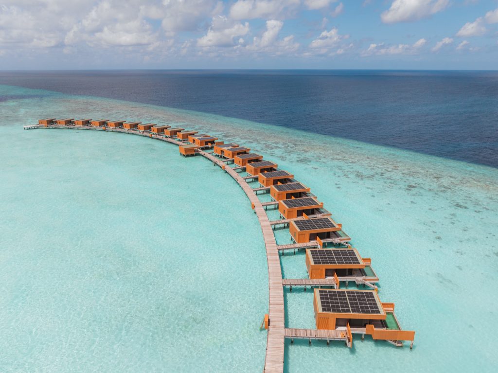Über Wasser gebaute Ocean Pool Villen auf Steg mit Holzbau und Solarpaneelen, türkisfarbenes Wasser und klarer Himmel