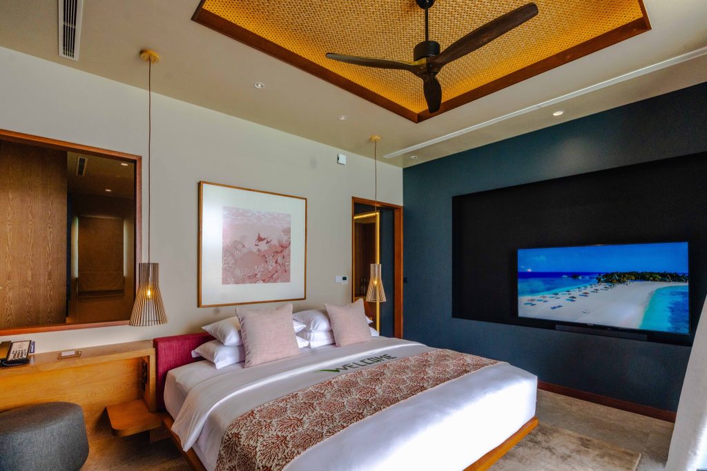 Modernes Hotelzimmer Ocean Pool Villa mit großem Bett, Holzakzenten und Flachbildfernseher mit Strandbild