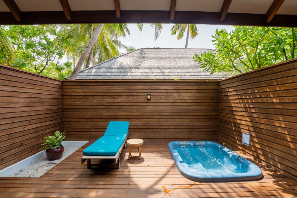 Privater Außenbereich der Sunset Jacuzzi Beach Villa mit Holzterrasse, kleinem Pool, Liege und tropischen Palmen