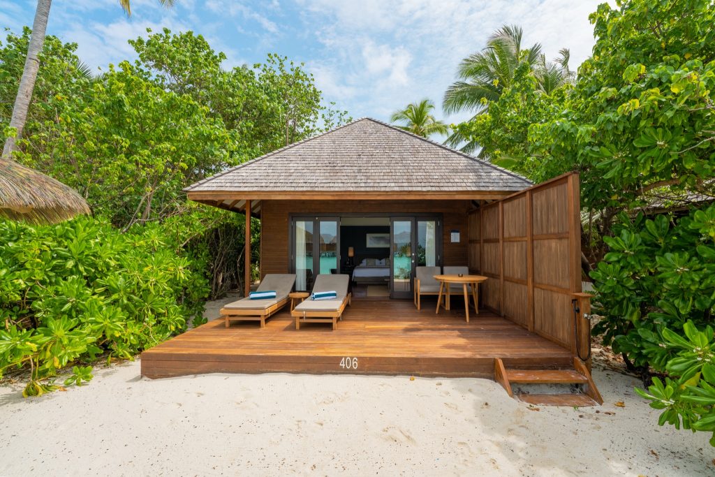 Bungalow mit Holzterrasse, Liegestühlen und Glasschiebetüren am Strand im Veligandu Maldives Resort Island