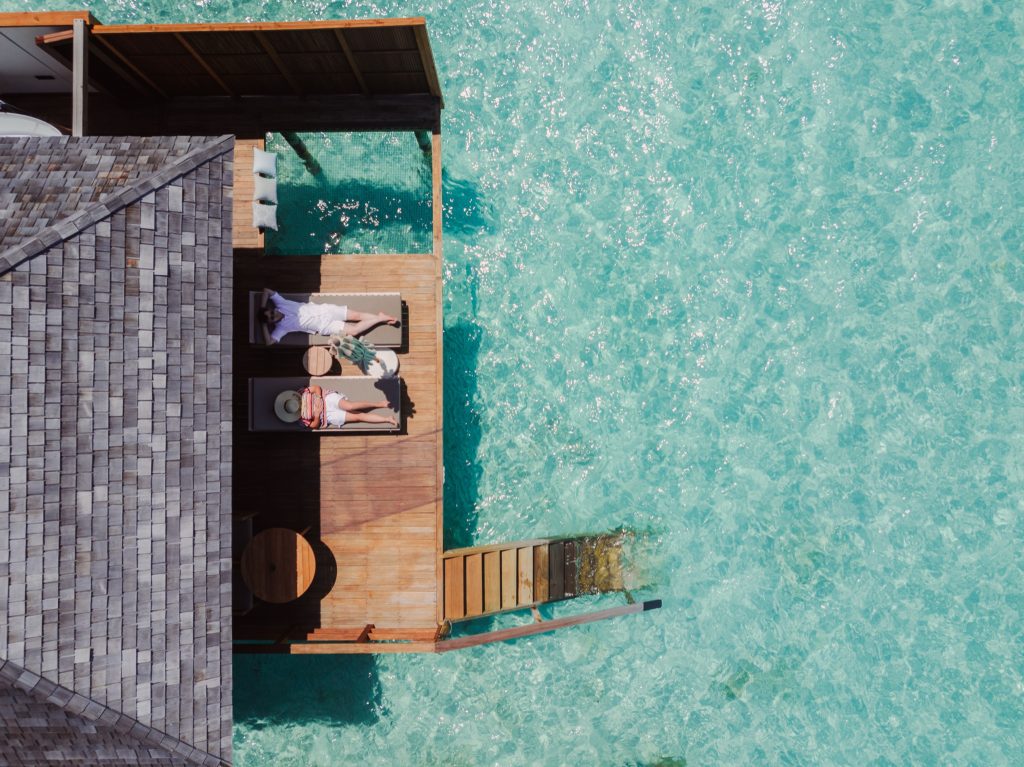 Terrasse der Sunset Ocean Villa mit Holzliegestühlen über türkisfarbenem Wasser und grauem Schindeldach