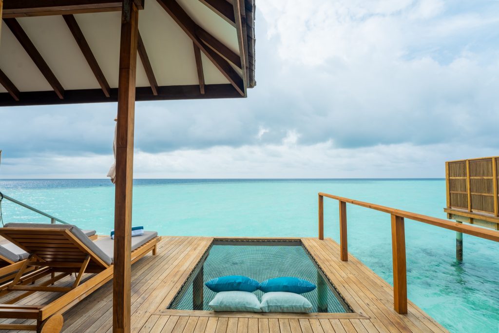 Terrasse der Sunset Ocean Villa mit Holzdeck, zwei grauen Sonnenliegen und blauer Netzliege über türkisfarbenem Wasser