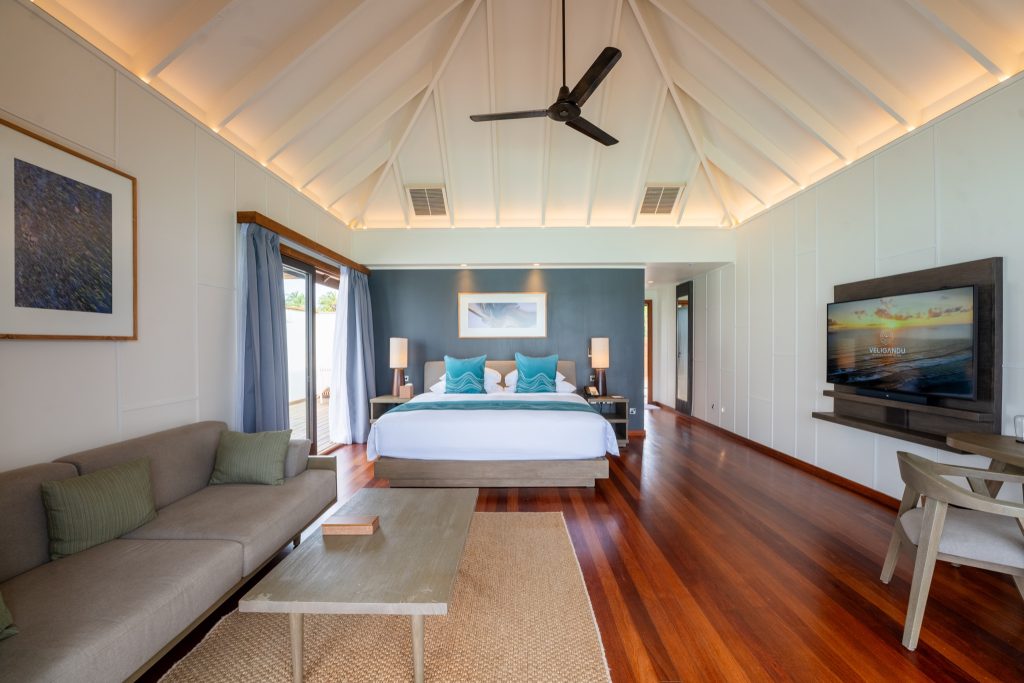 Modernes Hotelzimmer der Sunset Ocean Villa mit Doppelbett, grauem Sofa und großer Glas-Schiebetür