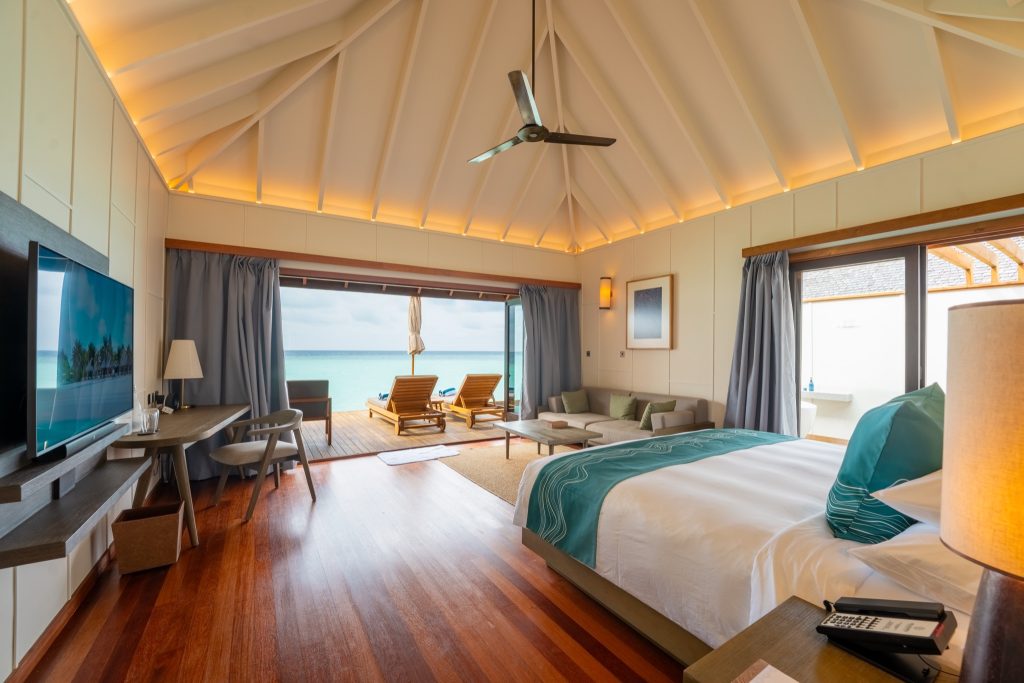 Zimmer der Sunset Ocean Villa mit Holzboden, großem Bett, Flachbildfernseher und Terrasse mit Sonnenliegen am Meer