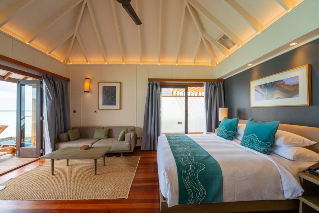 Geräumiges Zimmer der Sunset Ocean Villa mit Doppelbett, Sofa, Holzdeckenbalken und bodentiefen Fenstern