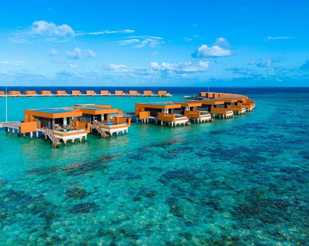 Wasserbungalows aus Holz auf Stelzen im türkisblauen Meer unter blauem Himmel mit weißen Wolken